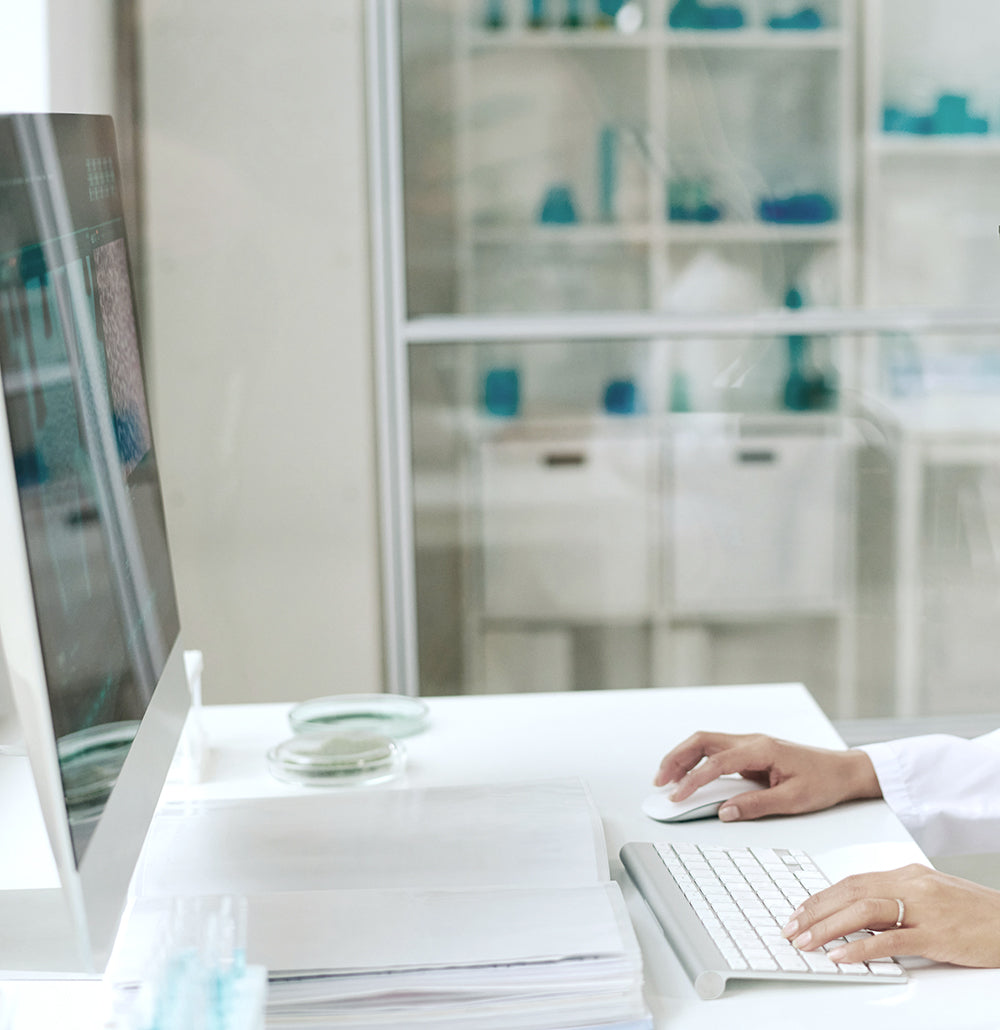 Person working at a desk with a computer and keyboard, with a blurred background of shelves.